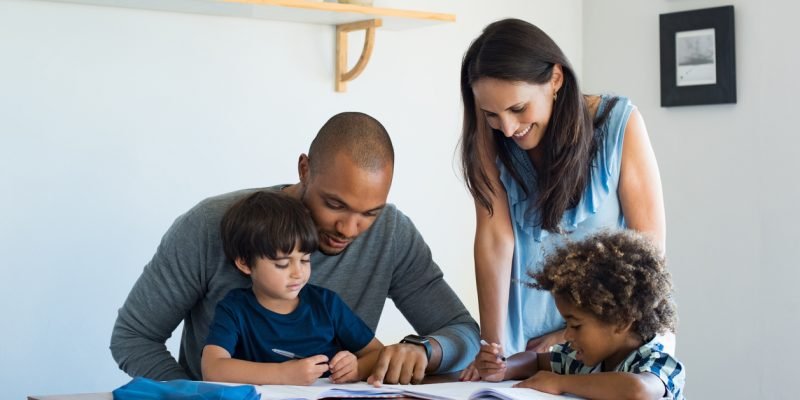Multiethnic parents helping children with their homework at home. Young father and mother helping sons study at living room. Little boys completing their exercises with the help of dad and mom.
