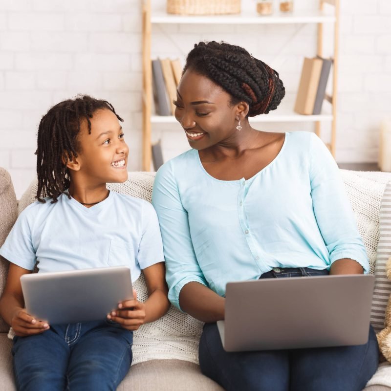 African Mother And Daughter Planning Trip, Choosing Travel Destination For Vacation Using Digital Tablet And Laptop
